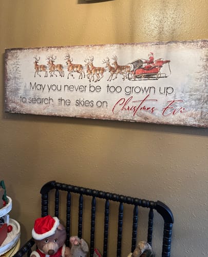 Customer's beautiful 'Search The Skies On Christmas Eve' sign hanging on a wall above a black bench and festive decor.