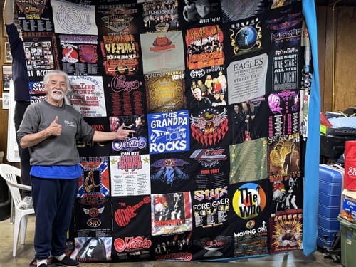 Customer proudly displaying their large Premium T Shirt Quilt made from a collection of concert t-shirts.