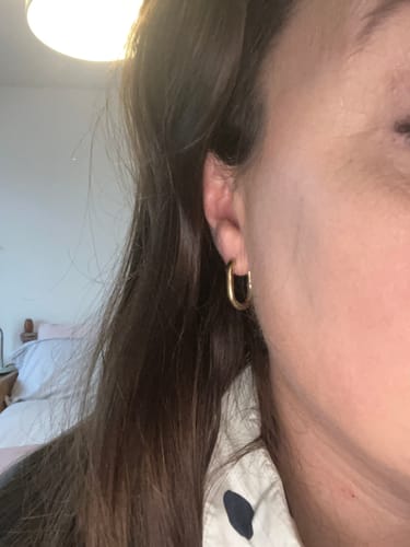 Close-up of a customer wearing a gold Oval hoop earring in their ear.