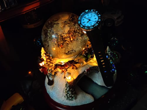 Reviewer's Oceaneva GMT watch with its bright blue full lume dial glowing in a dark room.