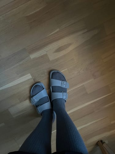 Recensentens grå Diasocks stödstrumpor som bärs med ljusa sandaler på ett trägolv.