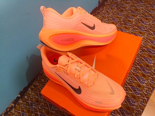 Customer's stylish orange Nike Vomero Plus shoes displayed on top of the product box.