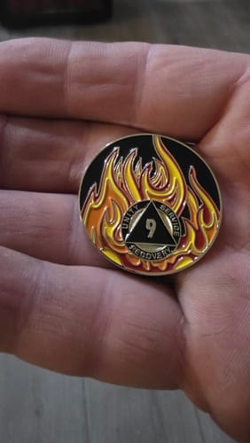 Customer holding the round 9 Year Sobriety Medallion with its colorful flame design in their palm.