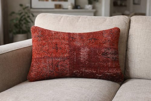 Reviewer's red over-dyed cushion cover with a distressed pattern resting on a beige sofa.