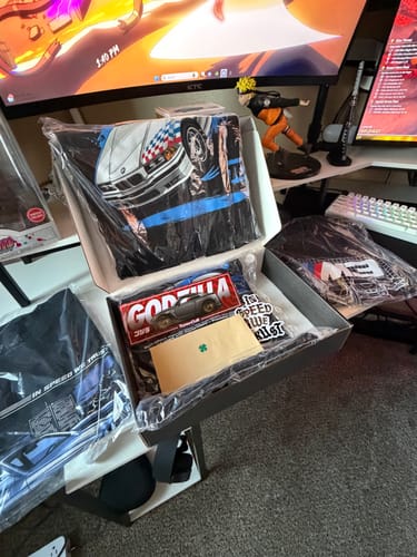 Customer's open TCG89 BLACK FRIDAY MYSTERY CASH BOX showing the graphic T-shirts and stickers inside.