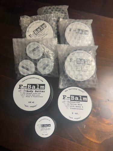 Customer's F-Balm products, including body butter and balms, on a wooden surface. Several items are still in bubble wrap packaging.