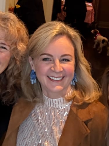 Reviewer smiling, wearing the blue beaded Avril Statement Earrings with a sparkly top and brown jacket.