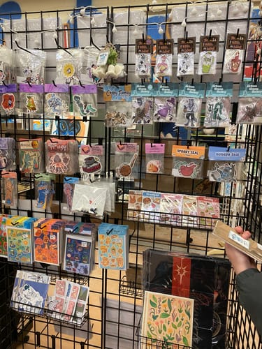 Customer's art sale booth displaying various colorful Cut to Shape Stickers in packaging on a black wire grid.