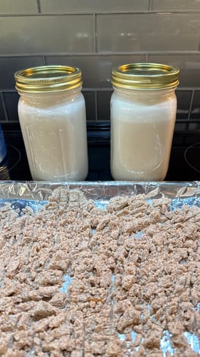 Customer's two Mason jars of homemade almond milk on a counter, with the leftover almond pulp drying on a tray in front.