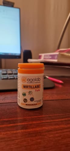 Cliente mostra il suo flacone di Mirtillase Forte su una scrivania di legno.