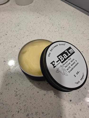 Customer's open tin of F-Balm tallow balm on a counter, showing the solid yellow balm with the lid beside it.