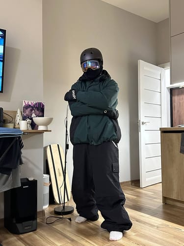 Reviewer wearing the dark green color block snow jacket with a helmet and goggles indoors.