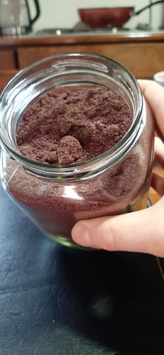 Cliente sostiene un frasco de vidrio abierto que contiene Maqui en polvo de color oscuro.