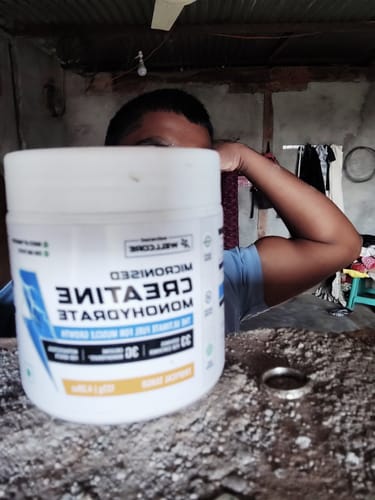 Reviewer holding a tub of Wellcore Creatine Monohydrate while flexing their bicep.