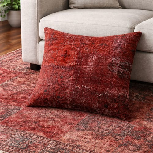 Customer's red patterned Hali Cushion Cover on the floor, leaning against a light-colored sofa in a living room setting.