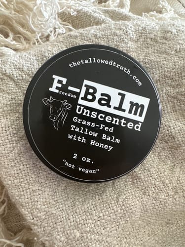 Customer's F-Balm Unscented tallow balm in a round, black tin on a woven cloth.