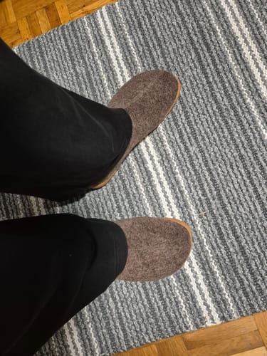 Asiakkaan jalassa ruskeat Vaistoa Toive -paljasjalkatossut kuvattuna ylhäältäpäin maton päällä.