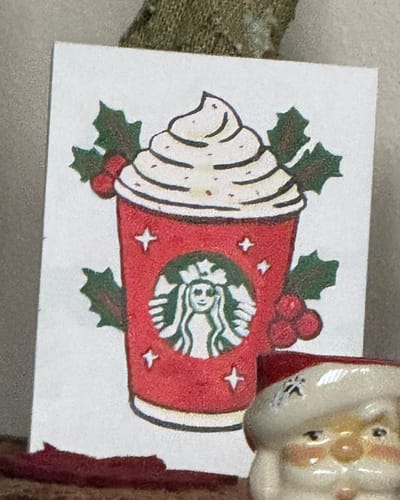Close-up of a customer's finished mini painting of a festive red coffee cup with whipped cream and holly.