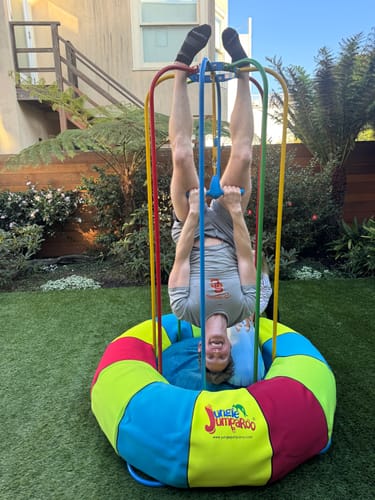Customer hangs upside down inside the colorful Jungle Jumparoo in a backyard setting.