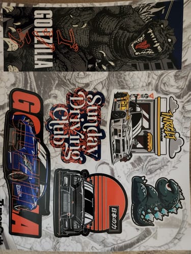 Customer's GODZILLA STICKER SHEET showing assorted colorful stickers of Godzilla and cars.