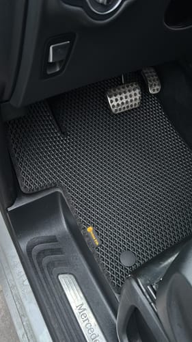 Recenzent pokazuje dopasowany, czarny dywanik samochodowy po stronie kierowcy.