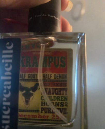 Close-up of a customer holding the square Krampus perfume bottle, showing the vintage-style label.