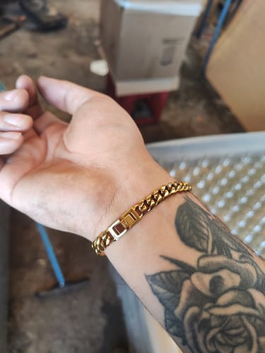 Primer plano de la Pulsera Cuban Oro en la muñeca tatuada de un cliente.