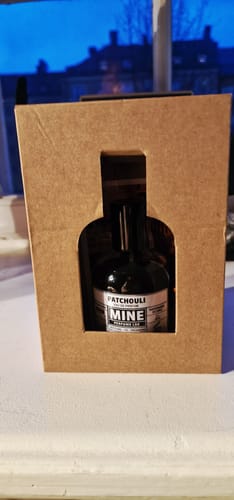 Recensore mostra il profumo PATCHOULI nella sua confezione in cartone marrone con apertura sagomata.