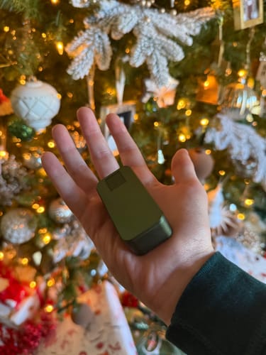 Customer holding a green Nano Case in their palm in front of a decorated Christmas tree.