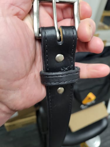 Reviewer's hand holding the 1.5" Antique Nickel #1 Buckle attached to a black leather belt.