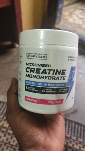 A customer holds a white tub of Wellcore Micronised Creatine Monohydrate in the Fruit Fusion flavor.