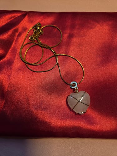 Customer's rose quartz heart pendant with gold wire wrap from the VIP Crystal Club on a red cloth.