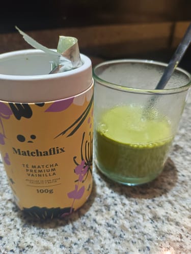 Un cliente muestra su Té Matcha Vainilla Premium junto a un vaso de té verde espumoso.