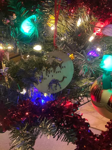 Reviewer's wooden Nativity Ornament with a camel and minaret scene hanging on a Christmas tree.