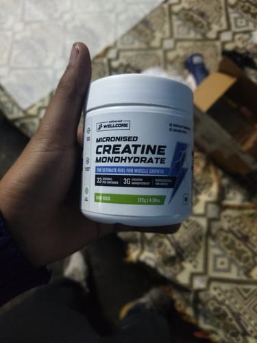 A customer's hand holding a white tub of Wellcore Micronised Creatine Monohydrate in the Kiwi Kick flavor.
