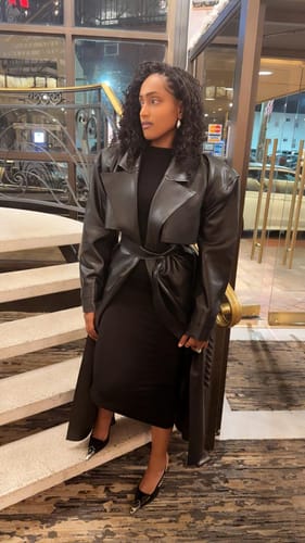 Reviewer on a staircase wearing the black NW Sculpt Mock Neck Dress, styled with a long leather coat.