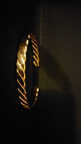 Customer's shiny gold Twisted Bangle Bracelet standing upright on a dark surface.