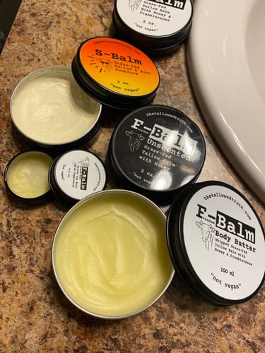 Customer's collection of balms, with an open tin of yellow F-Balm Body Butter on a bathroom counter.