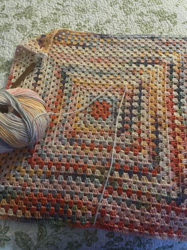 Reviewer's in-progress Hearthside Rainbow Blanket, showing the colorful gradient yarn from the kit and a crochet hook.
