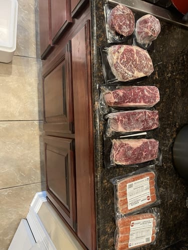 Customer's Choice Family Pack with vacuum-sealed steaks and free franks arranged on a dark granite kitchen counter.