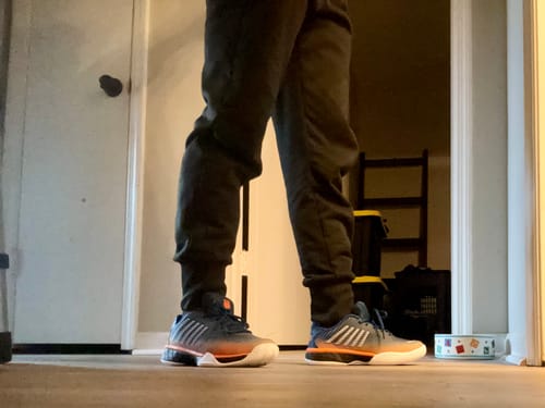 Customer standing on a wood floor wearing the grey and orange Hypercourt Express 2 tennis shoes.