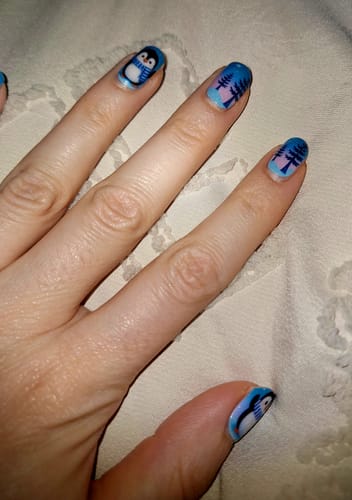 Hand einer Kundin, die die 'On Thin Ice' Nagelfolien mit süßen Pinguinen und Bäumen darauf trägt.