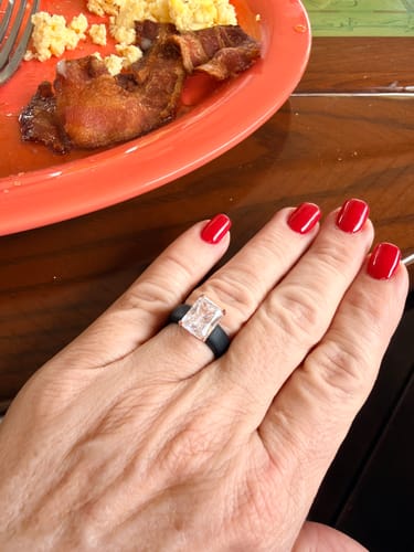 Customer's hand with red nails wearing the black silicone ring with a large, clear rectangular stone, shown over a breakfast plate.