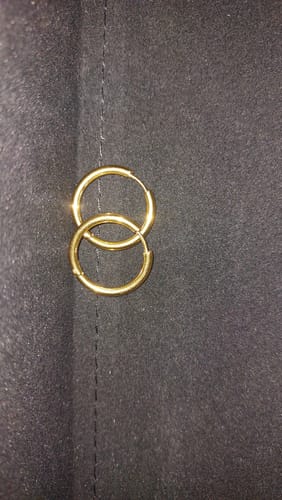 Customer's close-up of two small gold hoop earrings from their bundle on a black surface.
