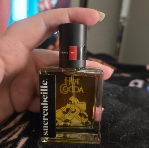 Customer holding a square bottle of Hot Cocoa perfume with dark amber-colored liquid.