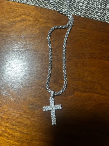 Customer's sparkling Moissanite Cross Pendant on a silver rope chain, laid out on a dark wooden table.