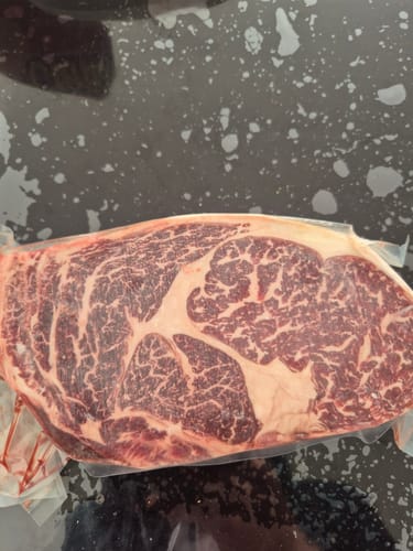 Cliente mostrando un corte crudo de Diezmillo Steak Black Brangus empacado al vacío, con abundante veteado.
