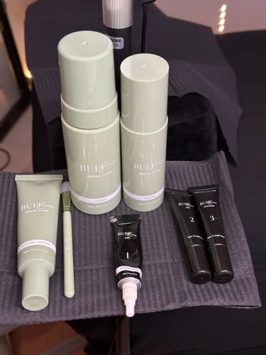 Customer's Hybrid Stain and Eyebrow Lamination products, including green bottles and black tubes, displayed on a towel.