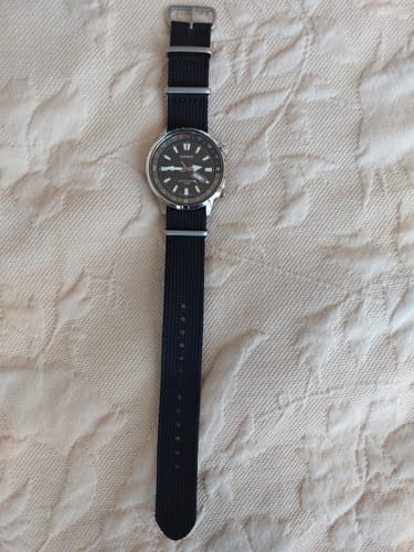 Cliente muestra la correa Nato negra en su reloj Casio, sobre una superficie de tela.