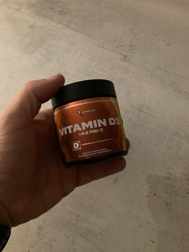 Reviewer holding the orange and black jar of Complex Vitamin D3+K2 MK-7.